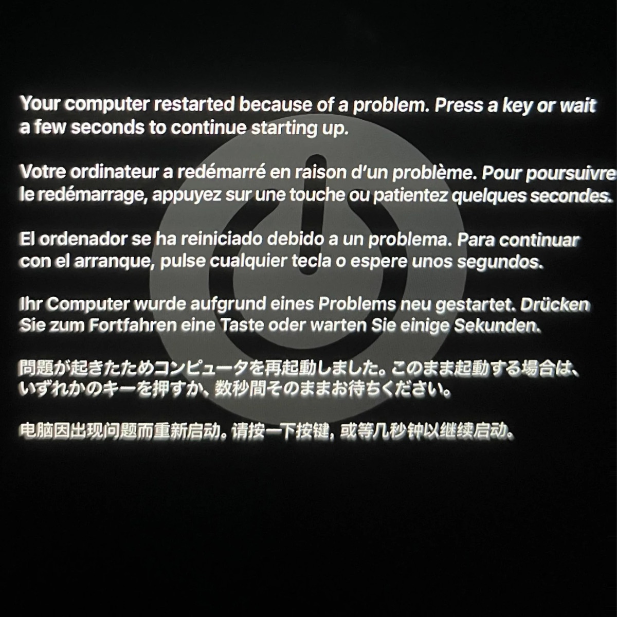 Mac screen with a power symbol and the message “Your computer restarted because of a problem. Press a key or wait a few seconds to continue starting up.” in English, French, Spanish, German, Japanese and Chinese.